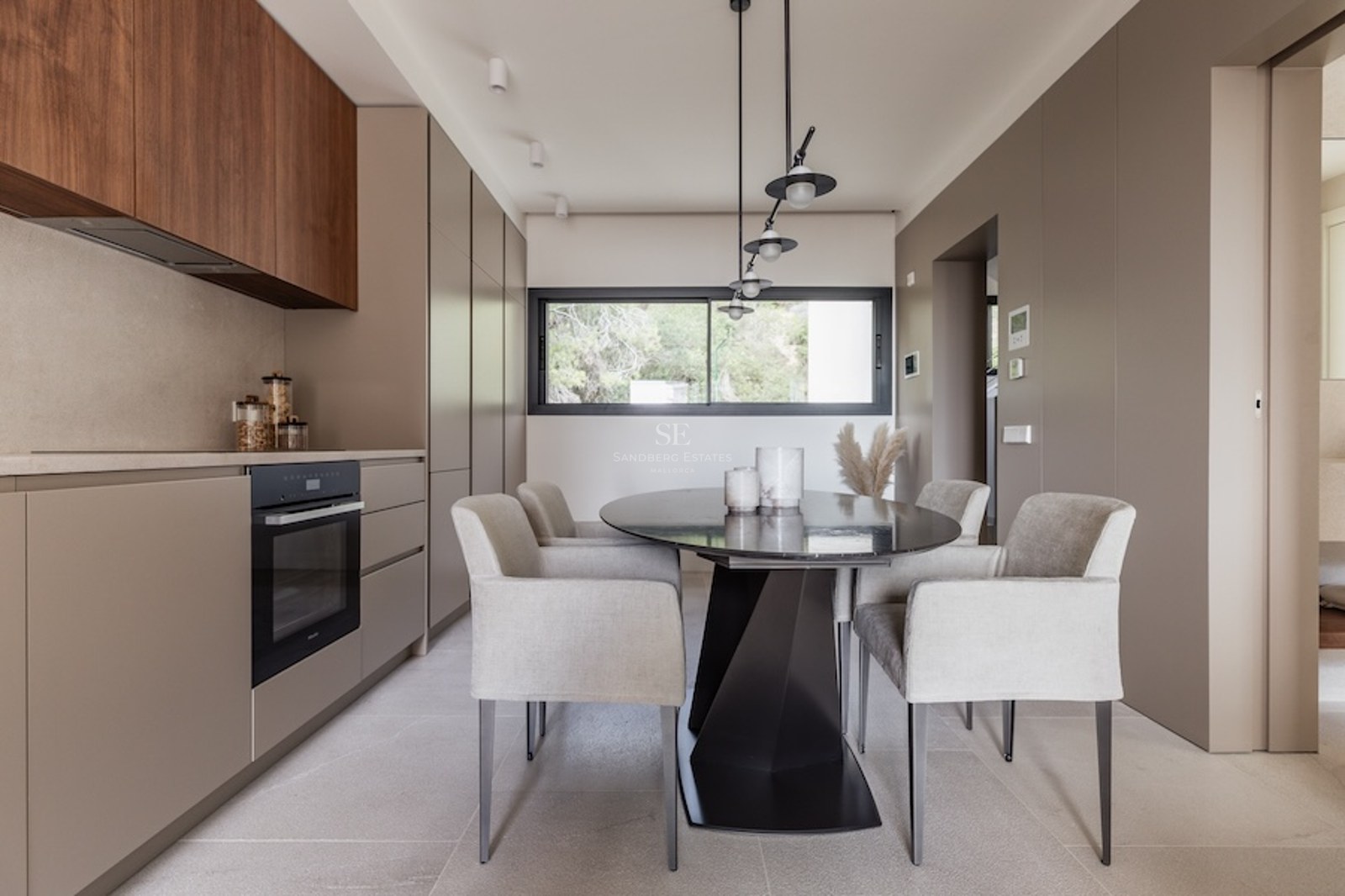 Modernes Esszimmer mit ovalem schwarzem Tisch, grauen Sesseln und taupefarbenen Schränken unter Designerleuchten.