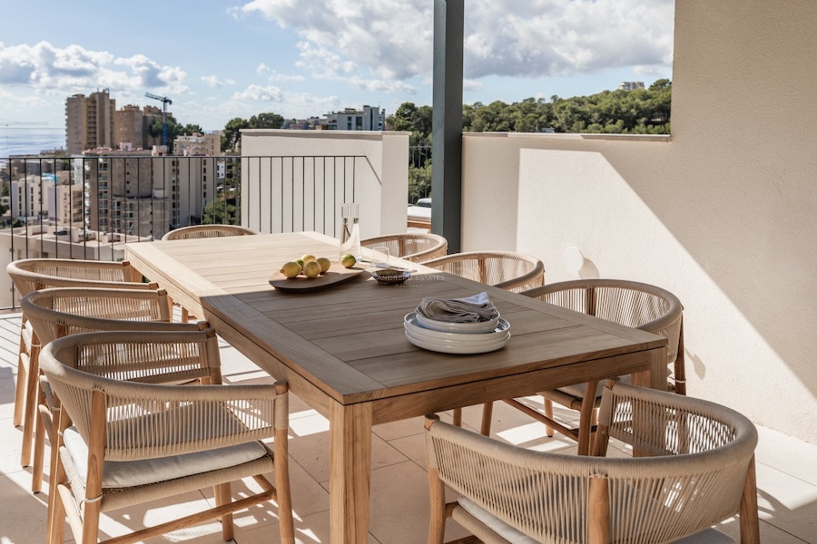 Moderne Terrasse mit Holztisch, geflochtenen Stühlen und Panoramablick auf Meer und Stadt.
