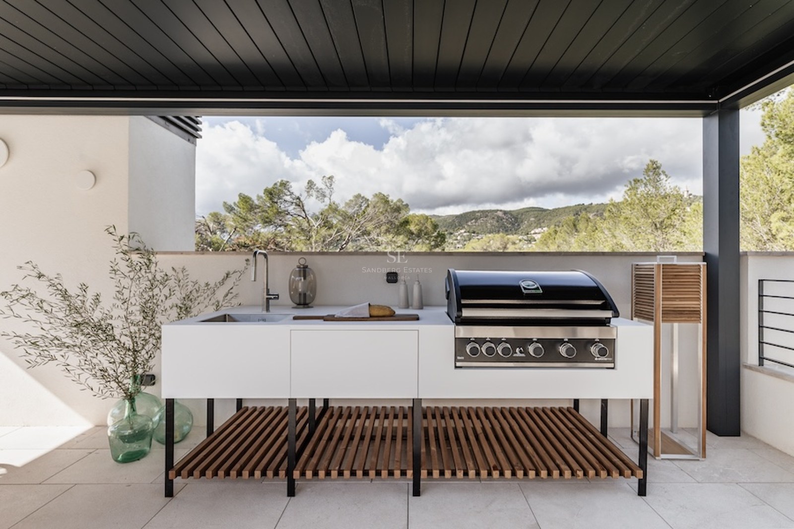 Moderne Außenküche mit Profi-Grill, Spüle und weißen Schränken auf einer Terrasse mit Blick auf die Berglandschaft.