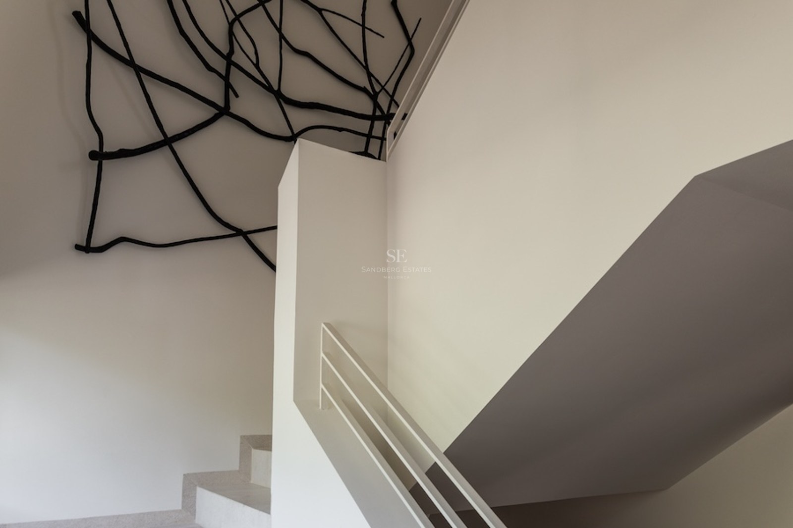 Weiße minimalistische Treppe mit einer schwarzen Ast-Skulptur an der Decke und den Wänden in einem hellen Raum.