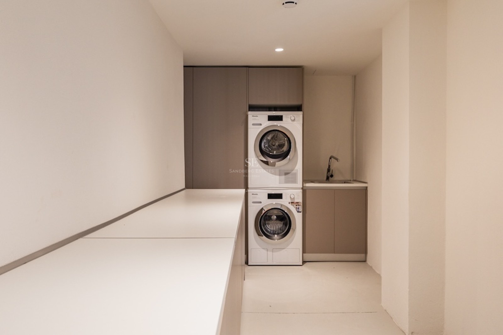 Gestapelte Miele Waschmaschine und Trockner in einem minimalistischen Hauswirtschaftsraum mit beigen Schränken.