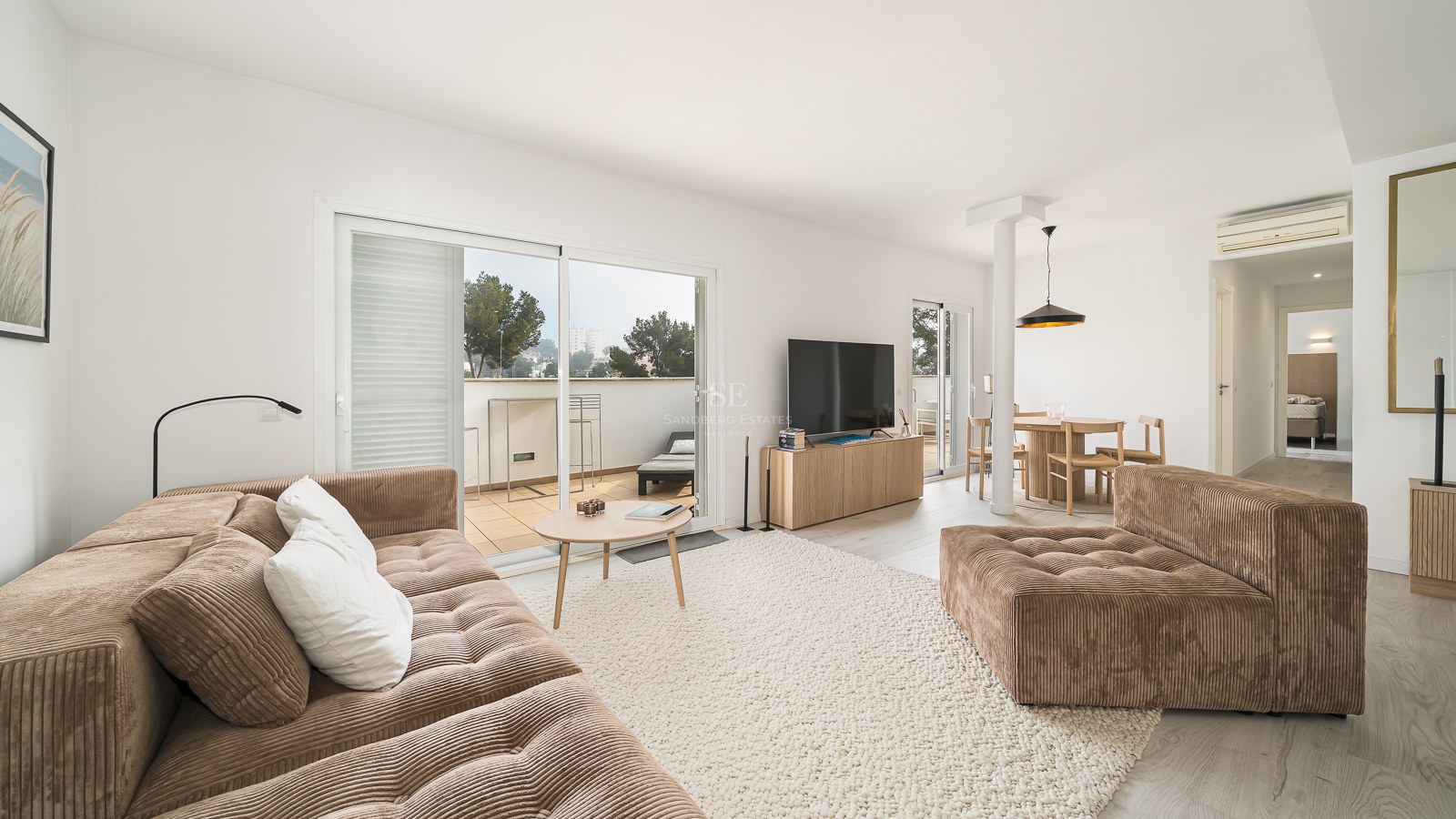Modern living room with a brown corduroy sofa, large rug, and sliding glass doors leading to a sunlit terrace.