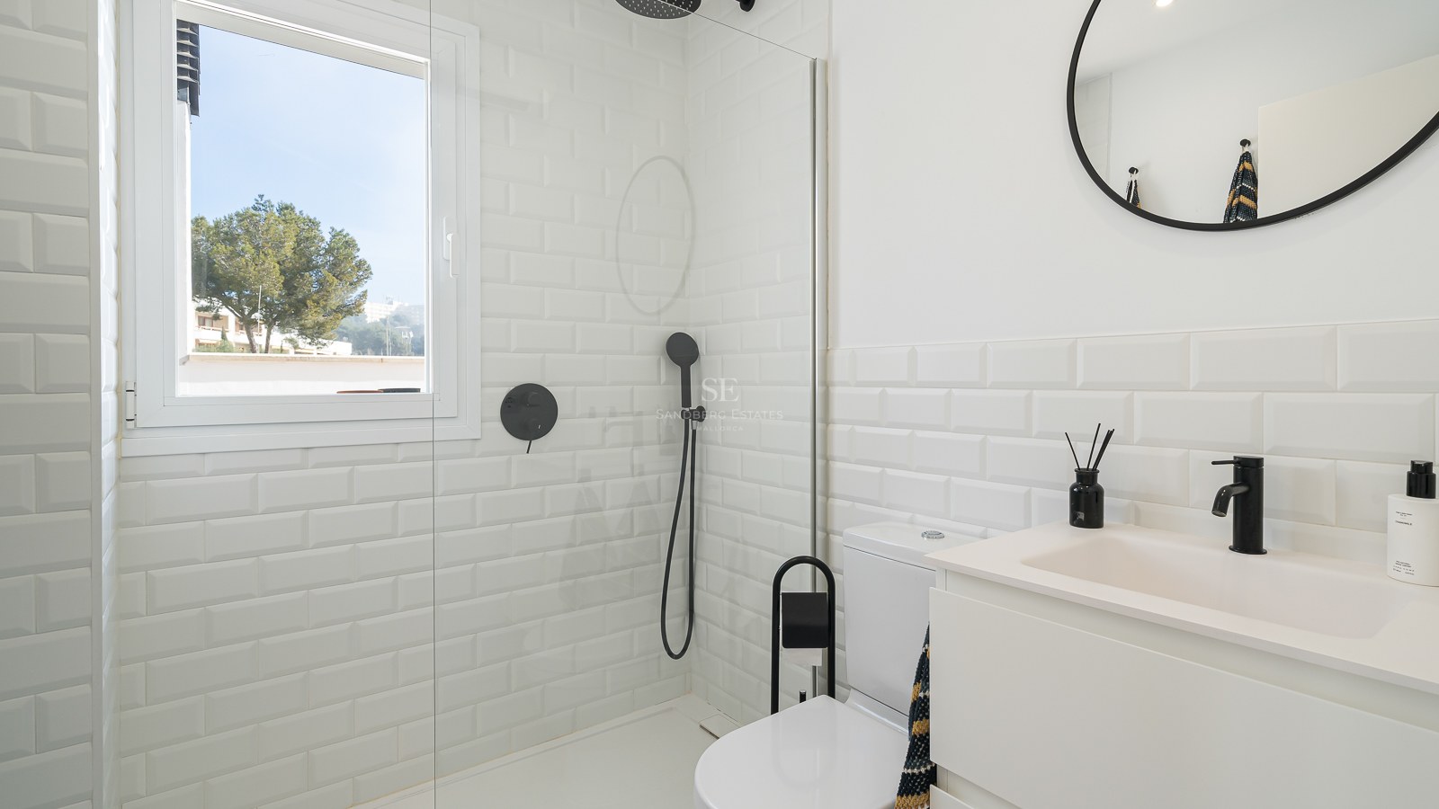 Bright bathroom featuring white subway tiles, a glass shower partition, and modern matte black fixtures.