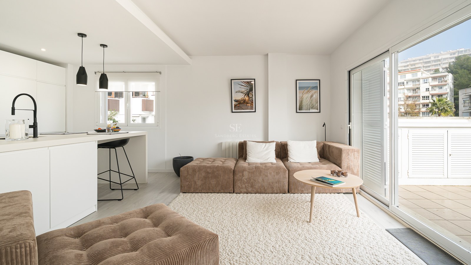 Bright living room with brown corduroy modular sofa, white textured rug, kitchen island, and large glass doors to a balcony.
