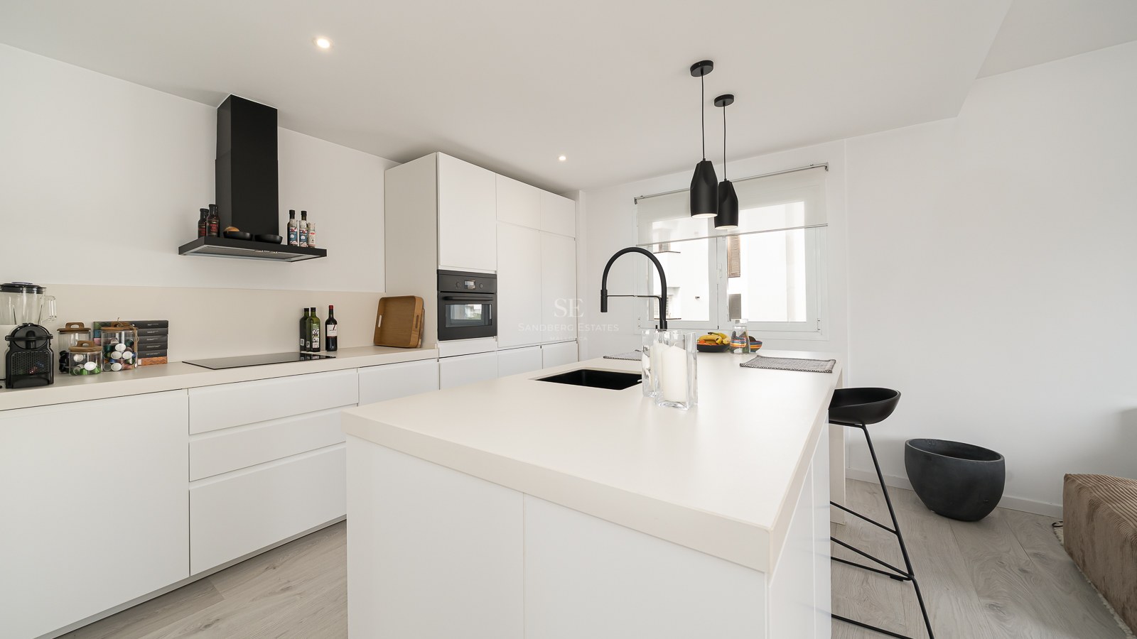 Modern white kitchen with a large island, black faucet, and sleek integrated appliances.