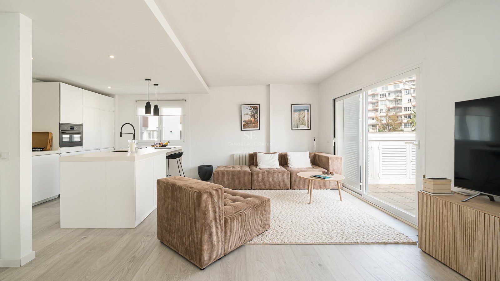Bright modern living room with a brown corduroy modular sofa, textured rug, and a minimalist white kitchen.