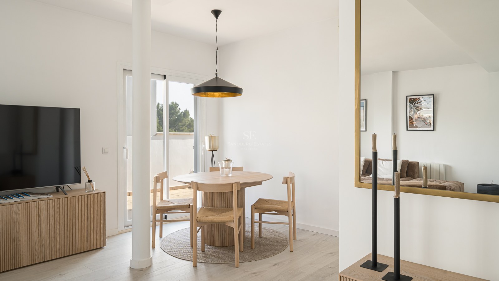 Bright dining area featuring a round wooden table, wicker chairs, black pendant lamp, and terrace access.