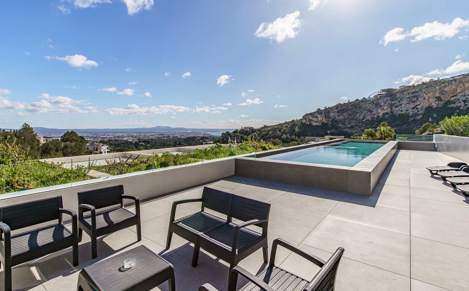 Terraza de lujo con piscina infinita, barandillas de cristal, muebles negros y vistas panorámicas al mar.