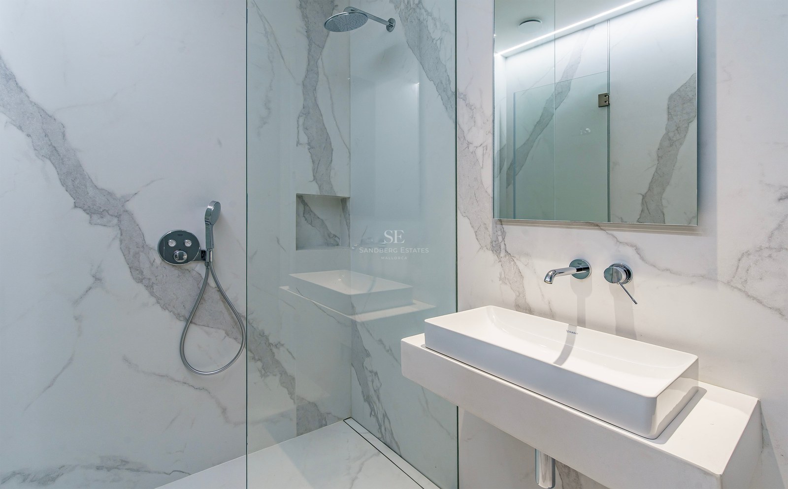 Baño moderno con azulejos efecto mármol blanco, ducha de cristal y lavabo minimalista con grifería cromada.