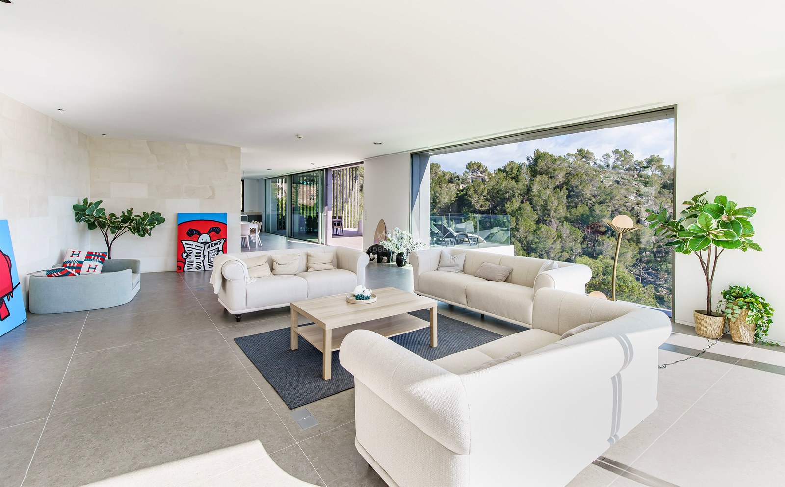 Amplio salón moderno con sofás color crema y grandes ventanales con vistas a un frondoso bosque verde.