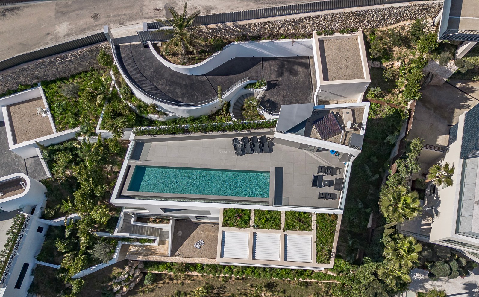 Vista aérea de una villa blanca moderna con piscina rectangular, tumbonas y una rampa de entrada curva.
