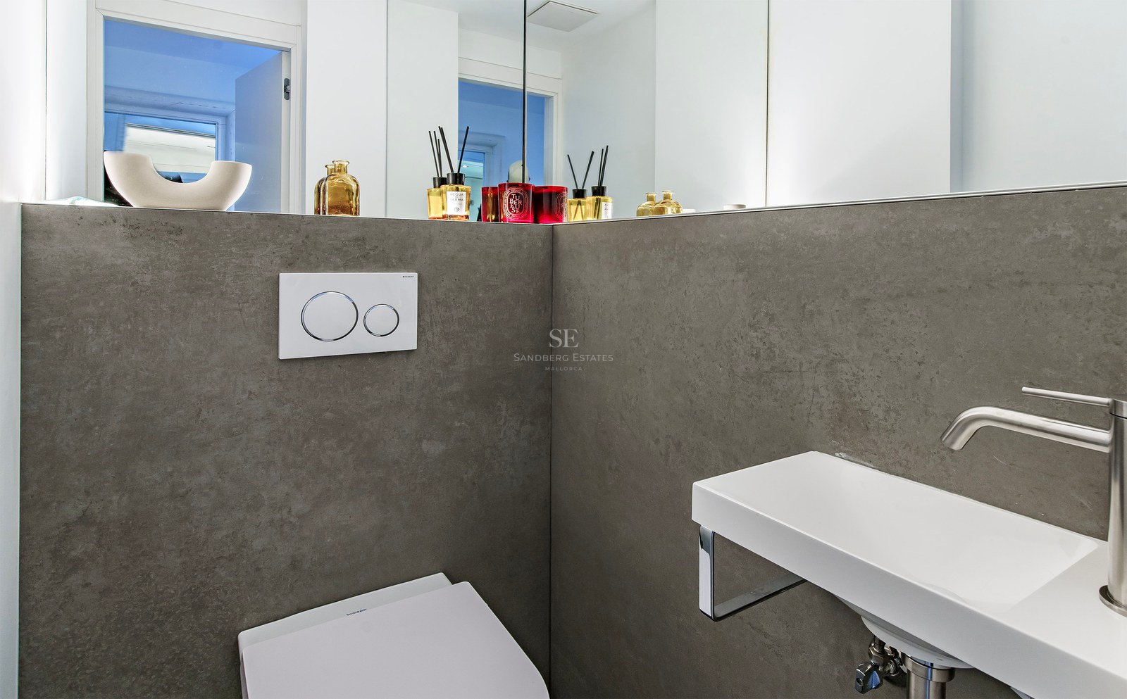 A minimalist bathroom featuring grey stone-effect walls, a slim white wall-mounted sink, and a large mirror.