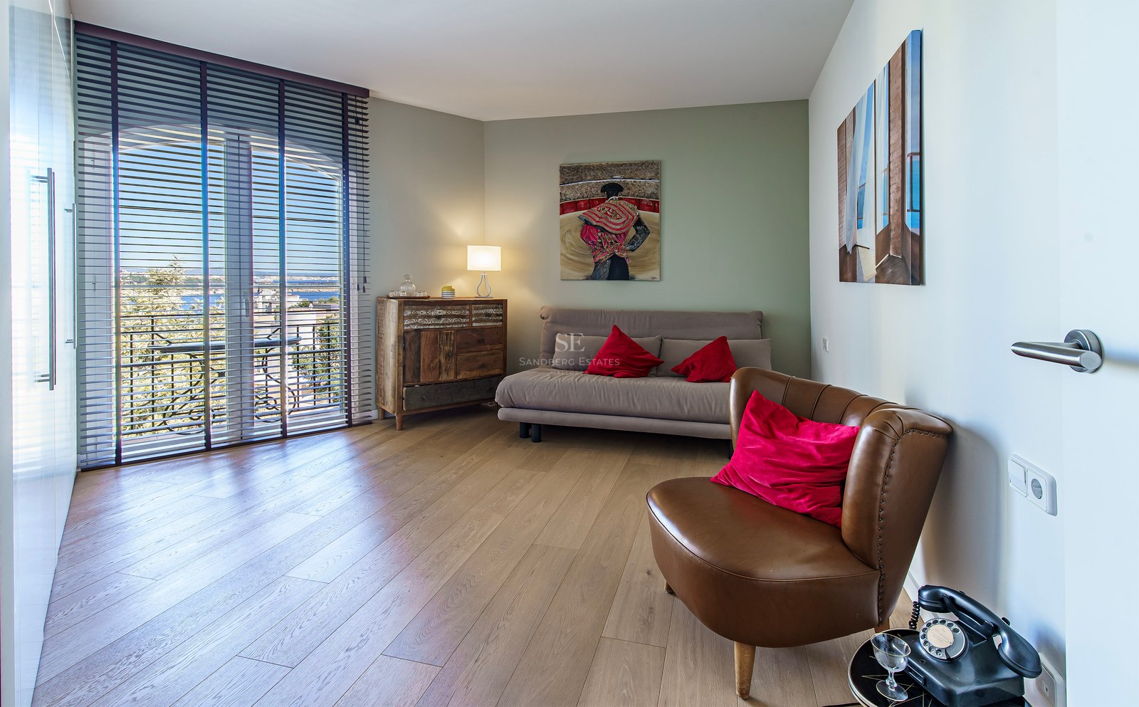 Contemporary bedroom with oak floors, a brown leather chair, sofa bed, and glass doors opening to a balcony.