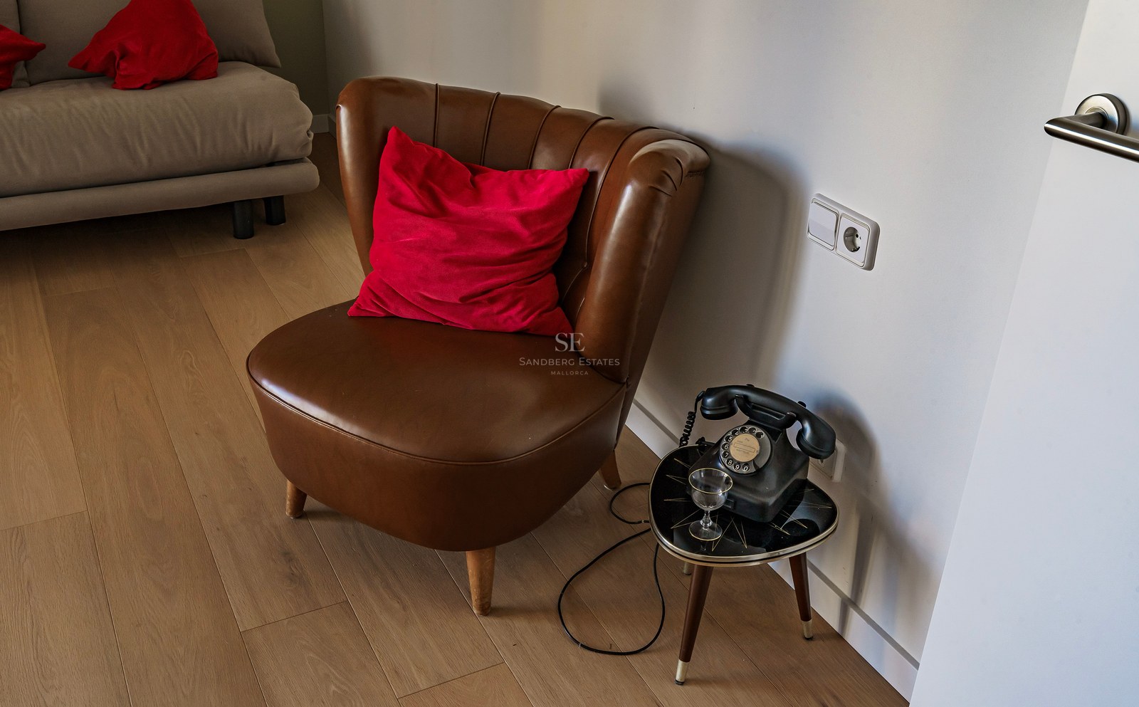 Fauteuil en cuir marron avec coussin rouge à côté d'un téléphone à cadran vintage sur une table basse.