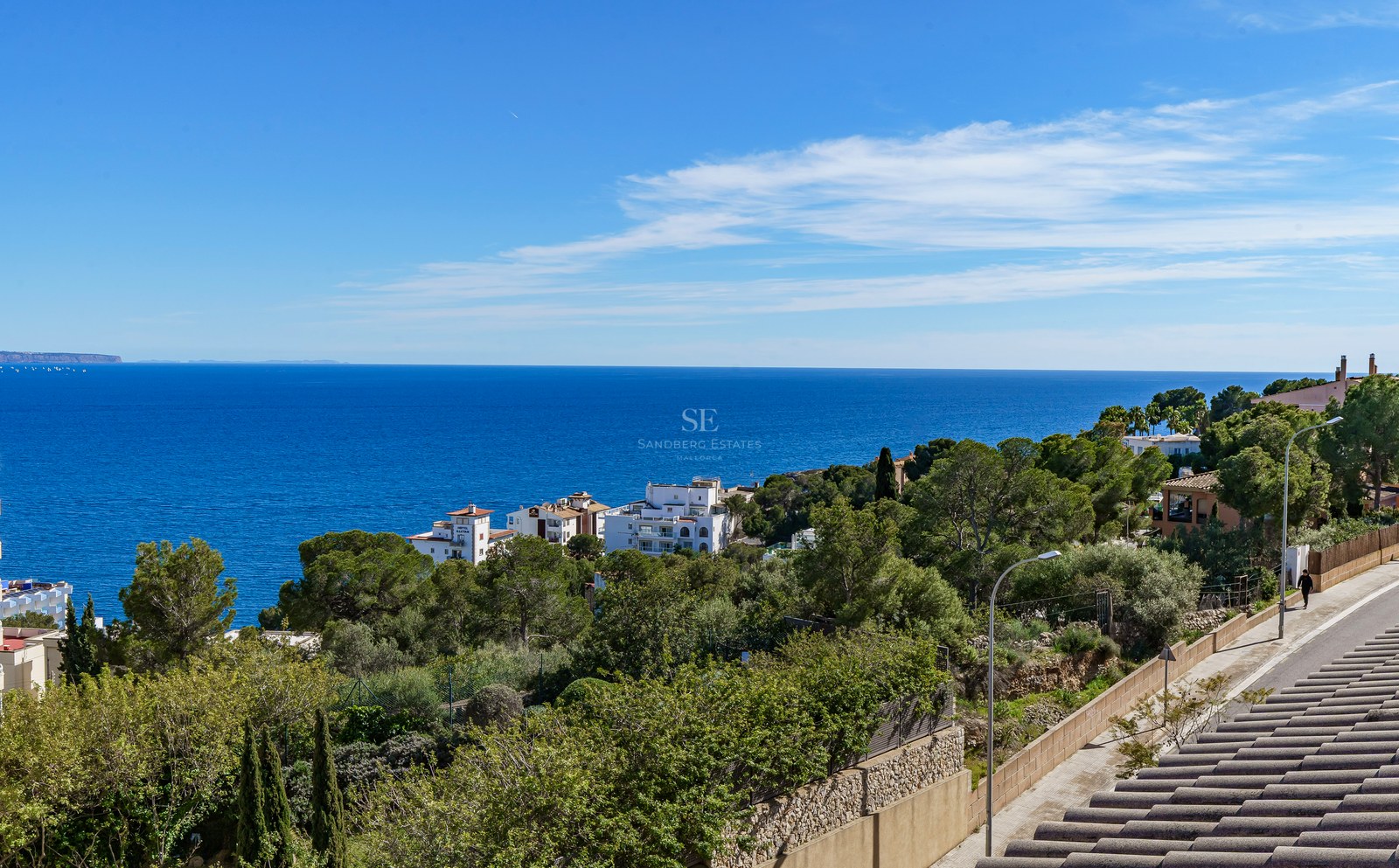Elevated panoramic view of the blue Mediterranean Sea, coastal pine trees, and white villas under a clear sky.