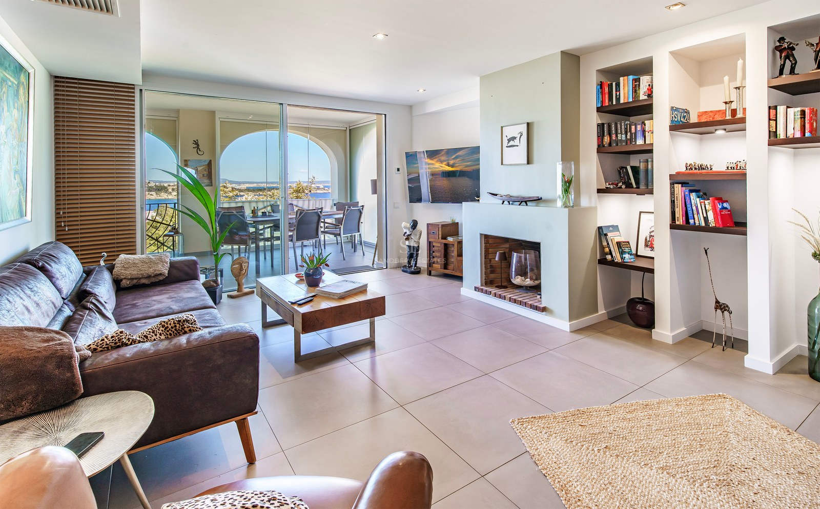 Bright living room featuring a leather sofa, integrated fireplace, and floor-to-ceiling sliding glass doors opening to a terrace.
