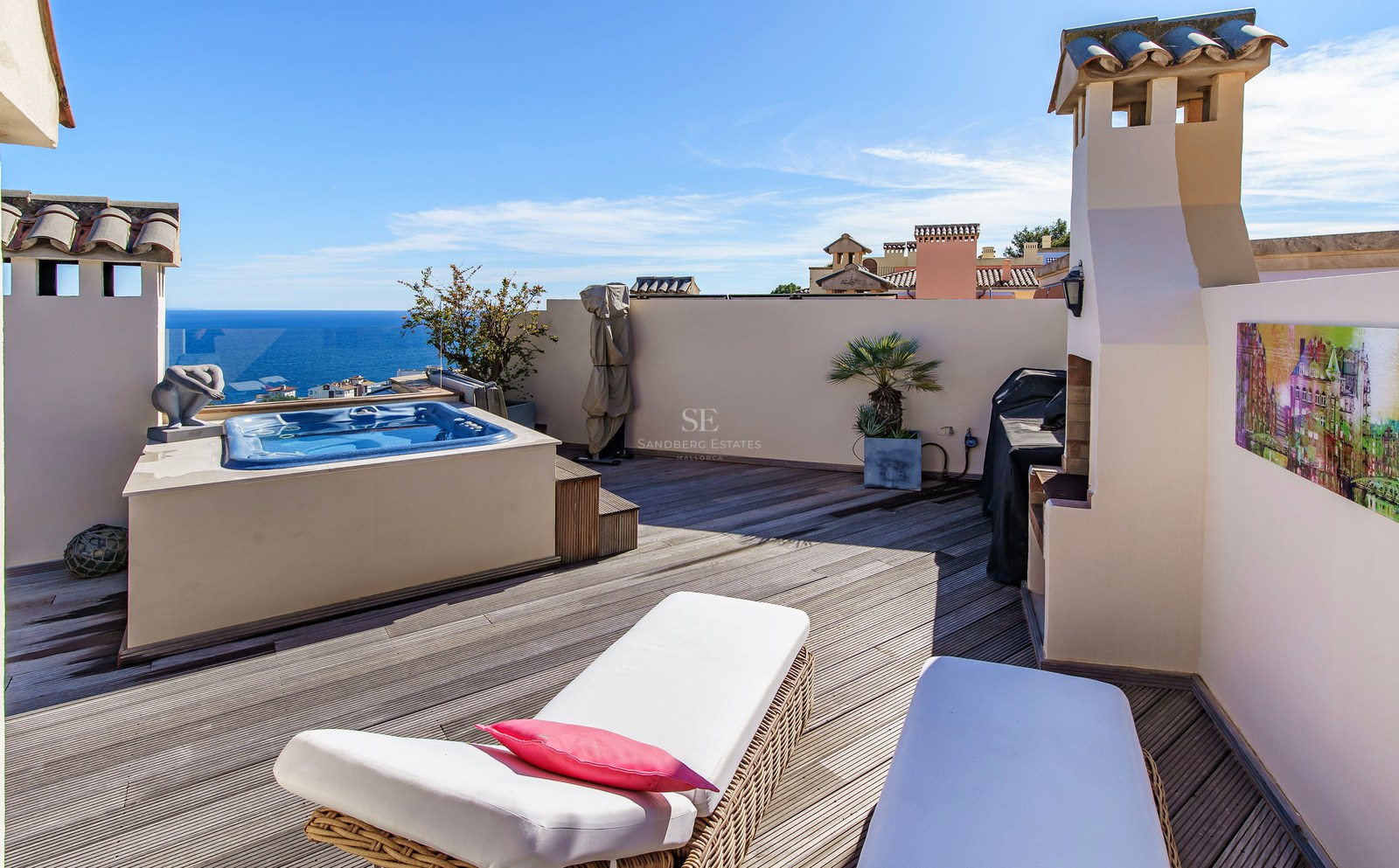 A sunny rooftop terrace with wooden decking, a built-in hot tub, white sun loungers, and panoramic views of the Mediterranean.