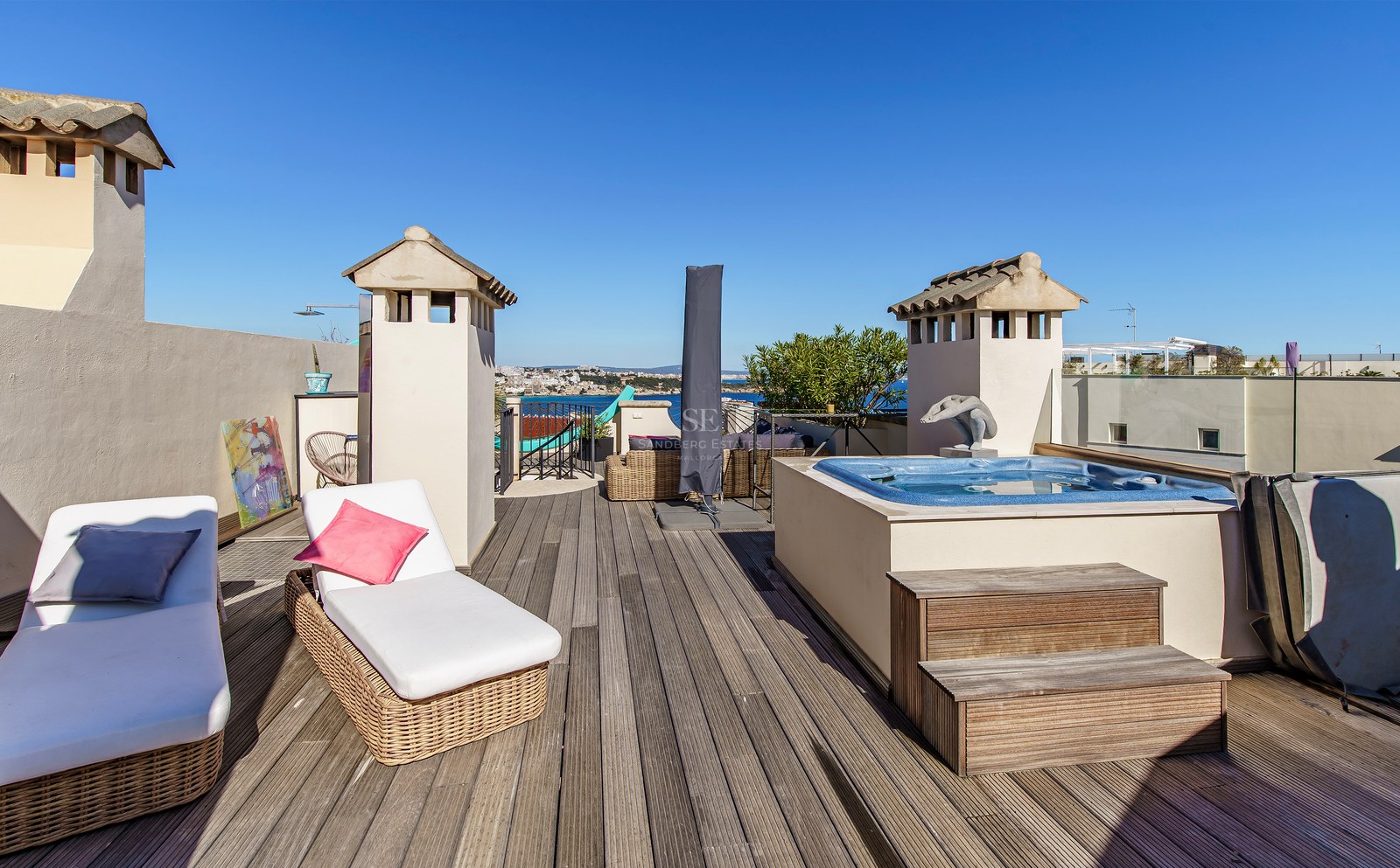 Rooftop wooden deck featuring a built-in hot tub, wicker sun loungers, and panoramic views of the Mediterranean coastline.