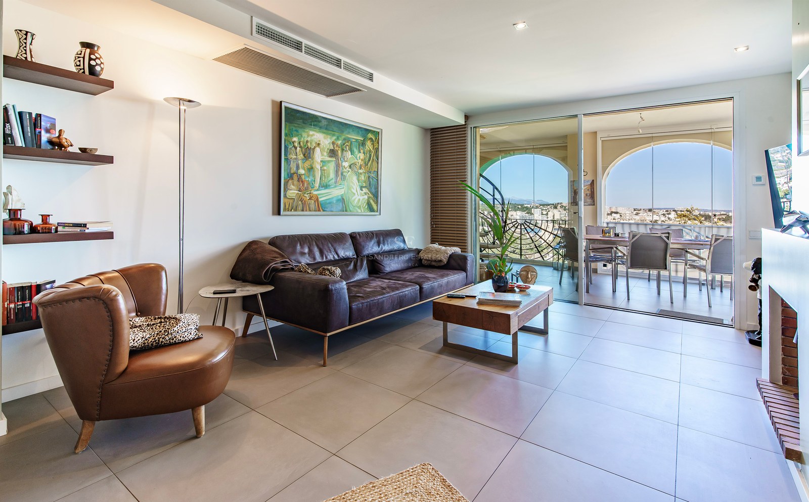 Modern living room with leather sofa and large glass doors opening to a terrace with panoramic coastal views.