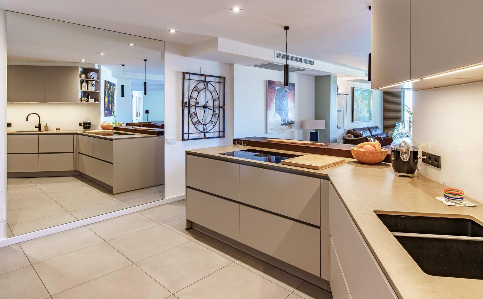 Contemporary open-plan kitchen with taupe cabinets, stone countertops, and a full-height wall mirror reflecting the room.