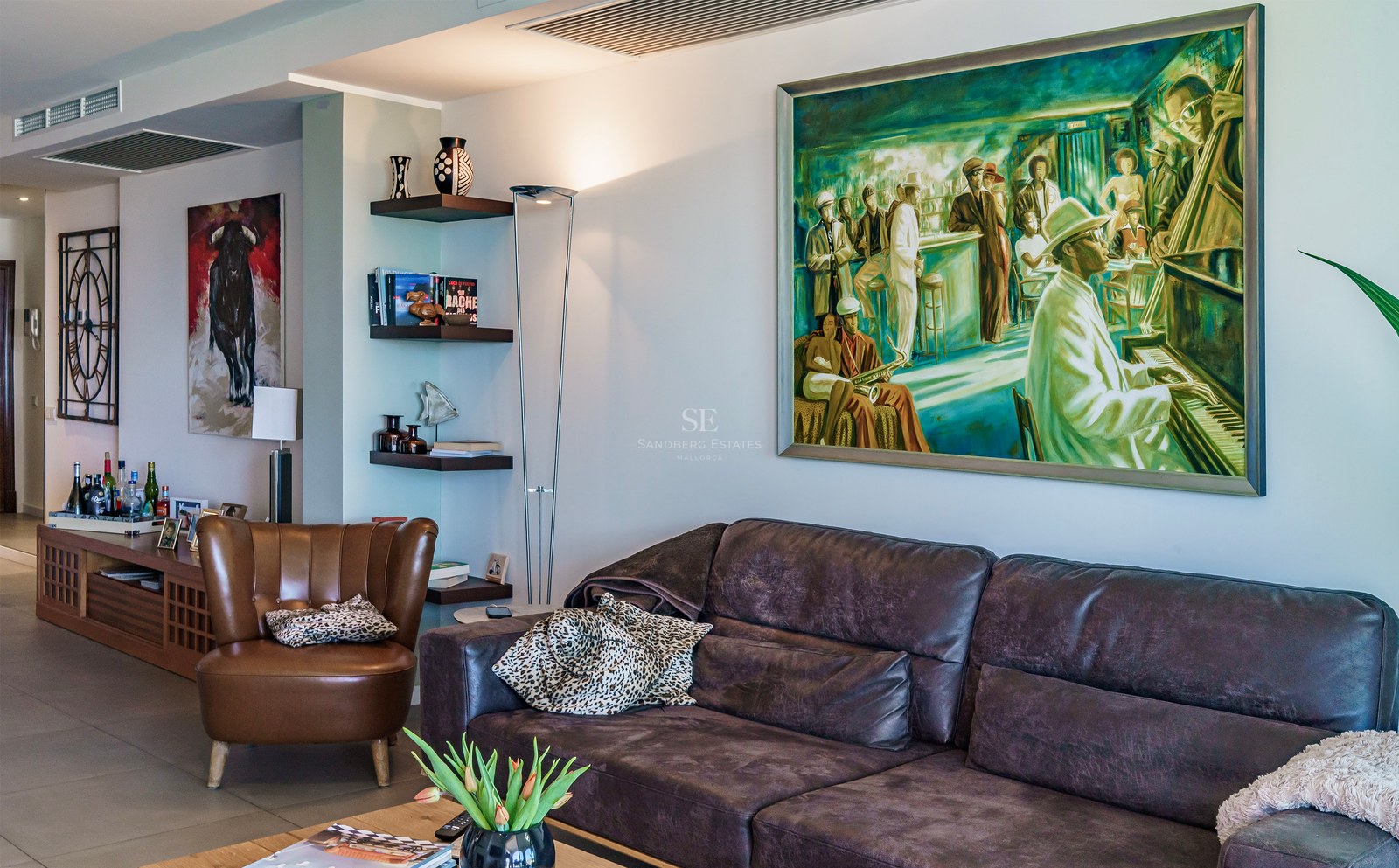 Salon contemporain avec canapé en cuir sombre, fauteuil cognac et grande peinture sur le thème du jazz.