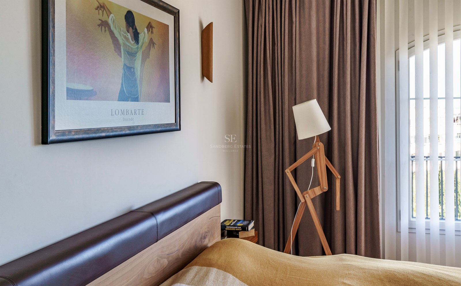 Gros plan d'une chambre avec une tête de lit en bois, un lampadaire design articulé et des rideaux taupe.