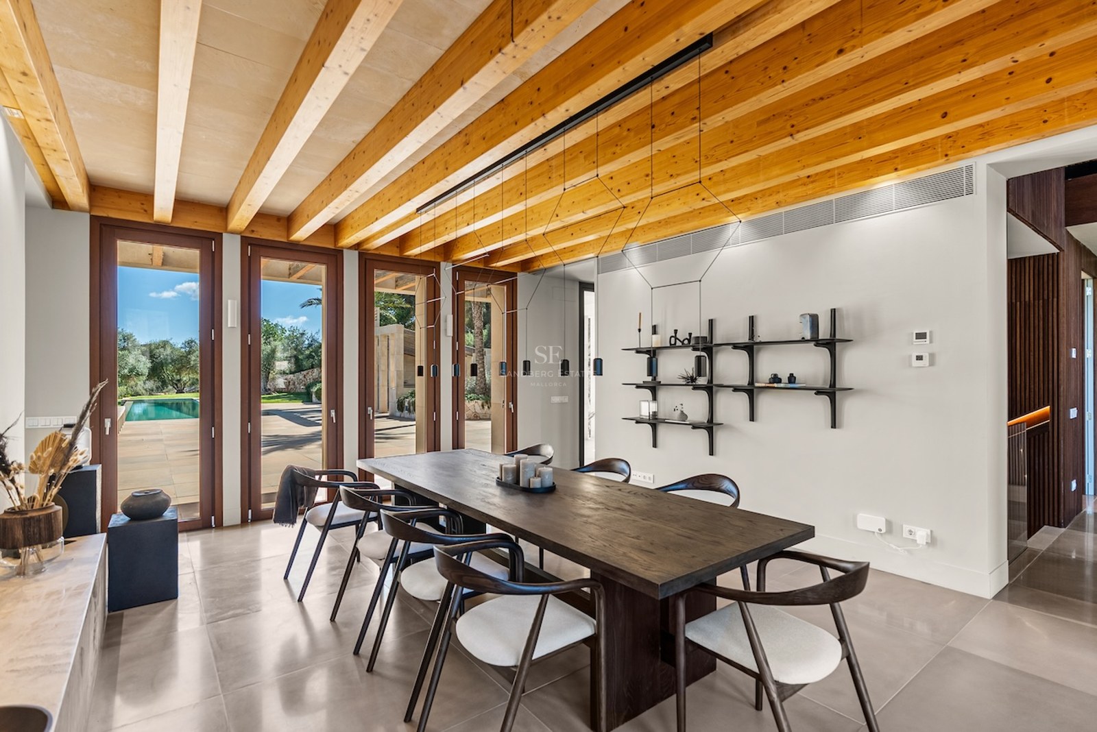 Modern dining room featuring a dark wood table, designer chairs, and a striking exposed timber beam ceiling in daylight.