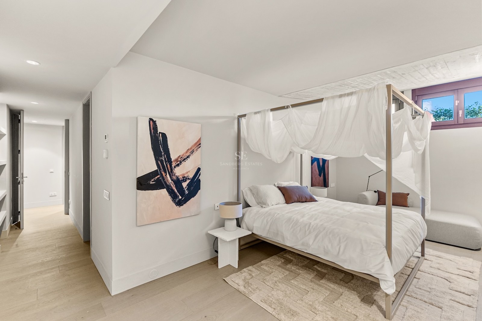 Bright bedroom featuring a four-poster canopy bed with white drapes, abstract art, and light wood flooring.