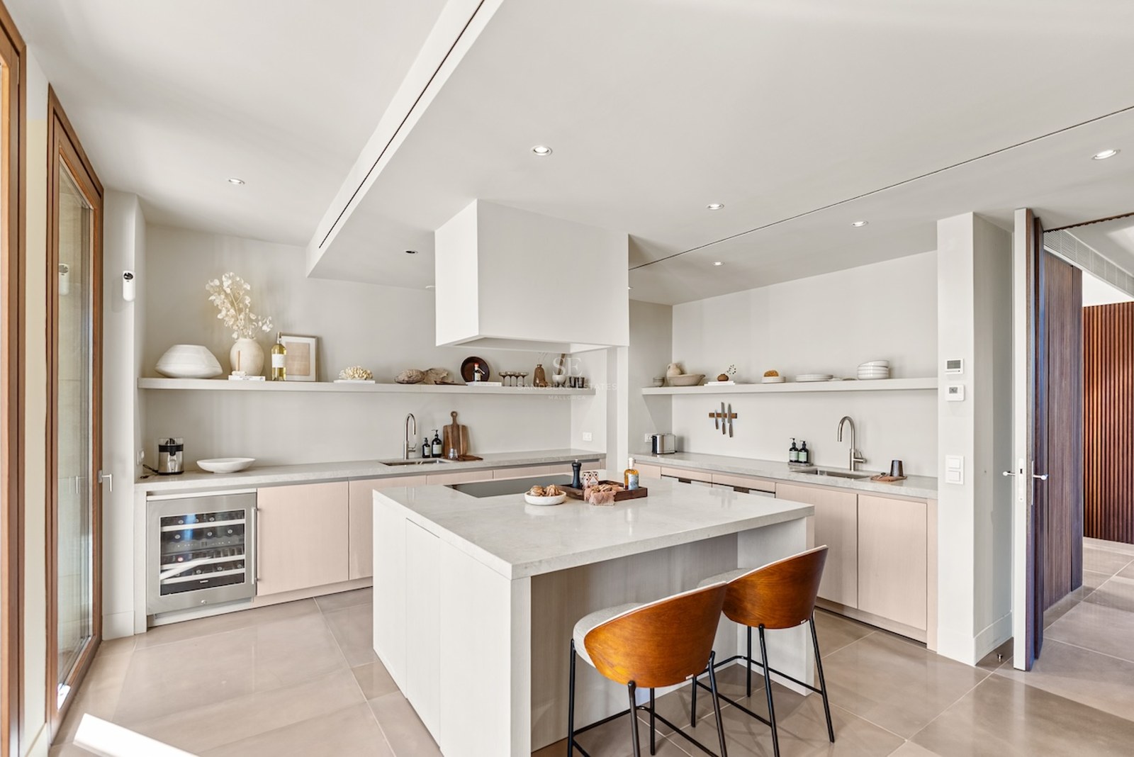 Bright modern kitchen with white island, stone countertops, wine cooler, and warm wood bar stools.
