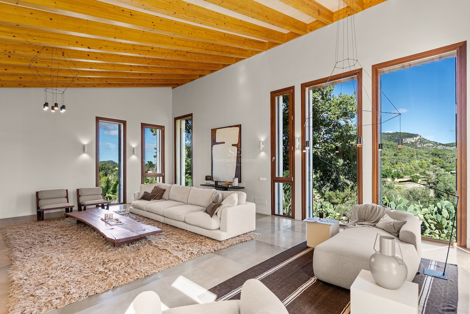 Spacious modern living room with wooden beamed ceilings, white sofas, and large windows looking out to mountains.