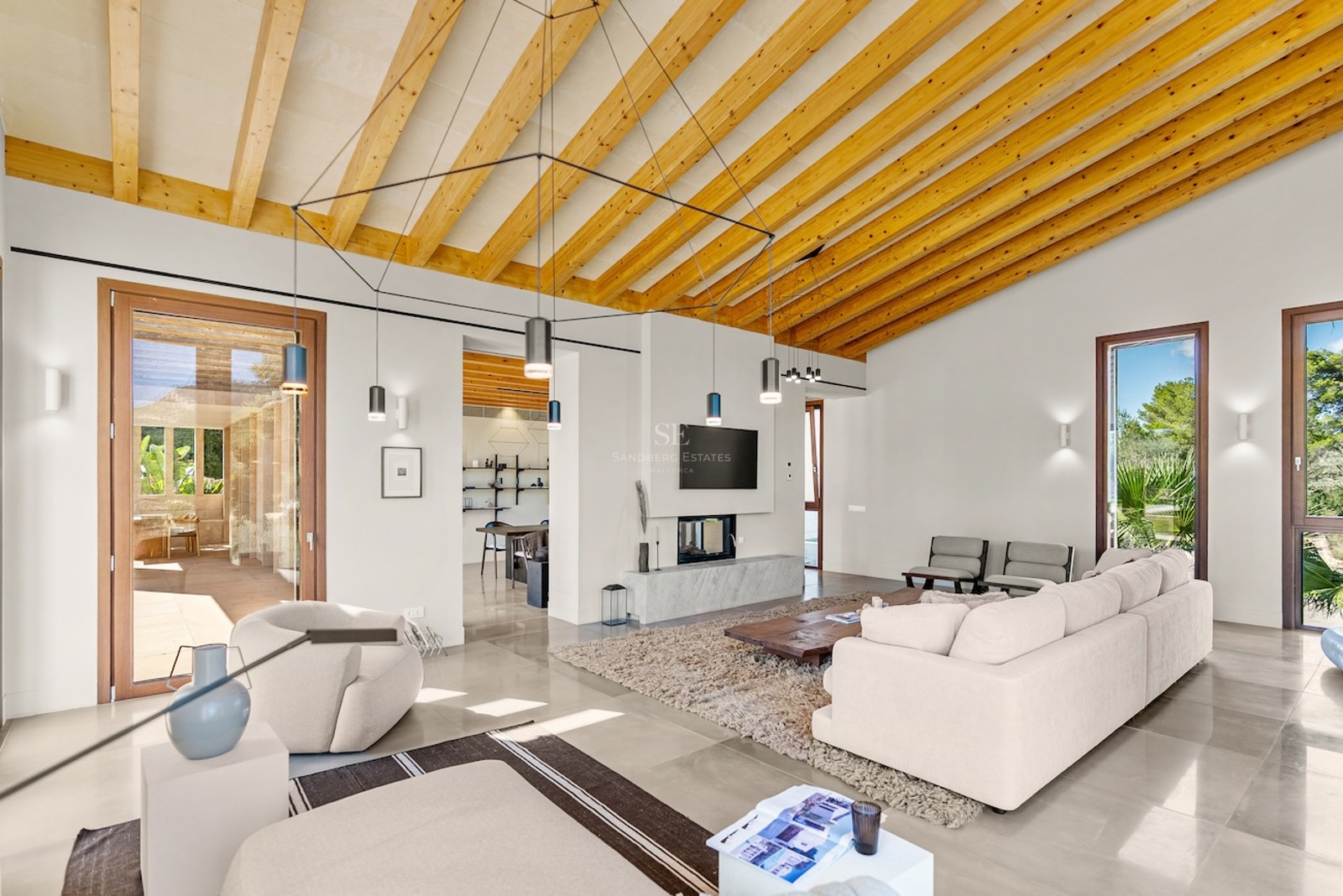 Bright living room with vaulted wood beam ceiling, cream sofas, modern fireplace, and large glass doors to a terrace.
