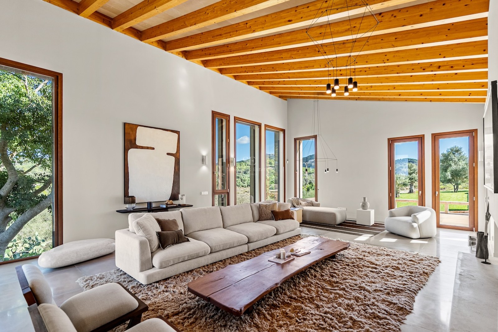 Bright living room with high wooden ceilings, cream sofa, live-edge wood table, and large windows viewing nature.