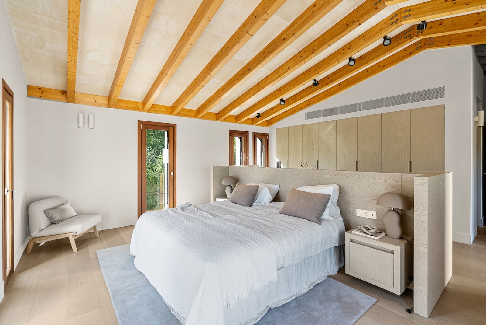 Modern master bedroom with vaulted ceiling, wooden beams, large bed, and built-in wardrobes.