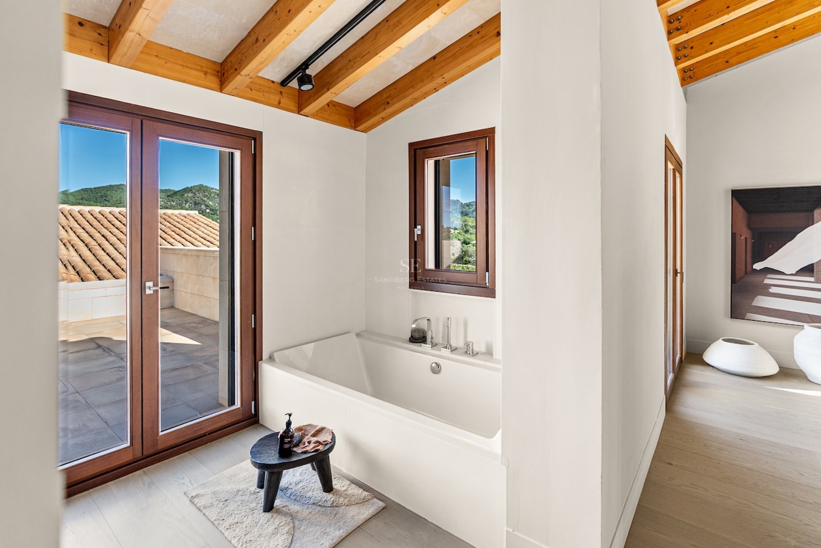 White built-in bathtub under a wooden beam ceiling with access to a terrace and mountain views.