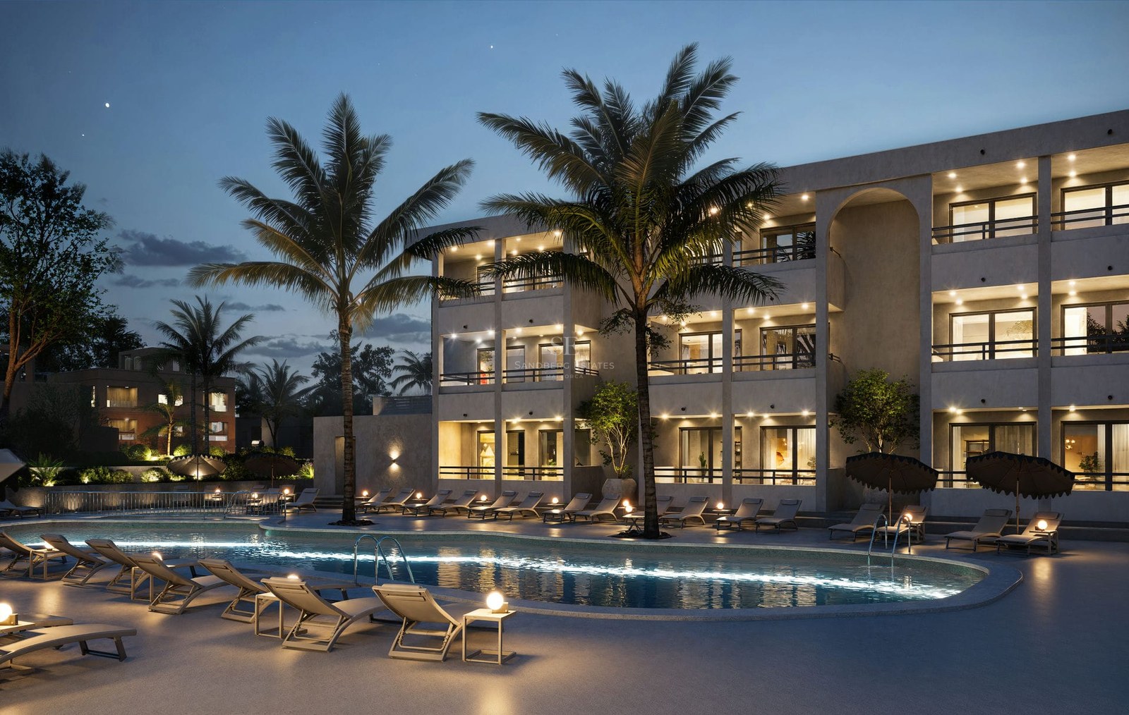 Large illuminated swimming pool with lounge chairs and palm trees in front of a modern apartment building at dusk.