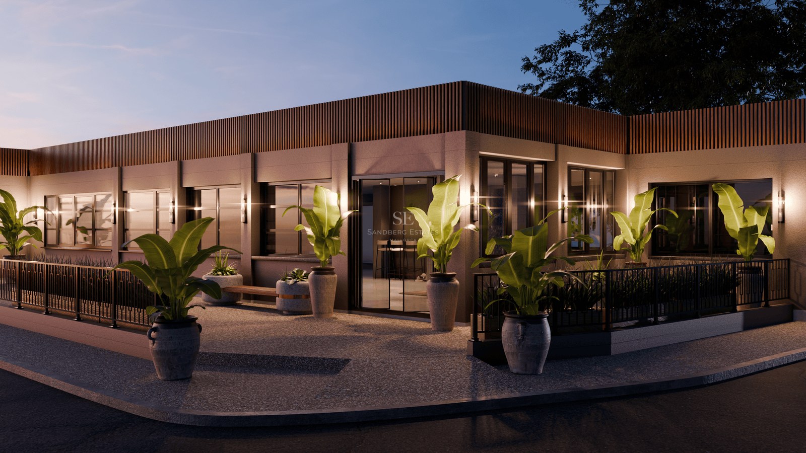 Modern building exterior at evening with warm wall lights and large green plants in stone pots.