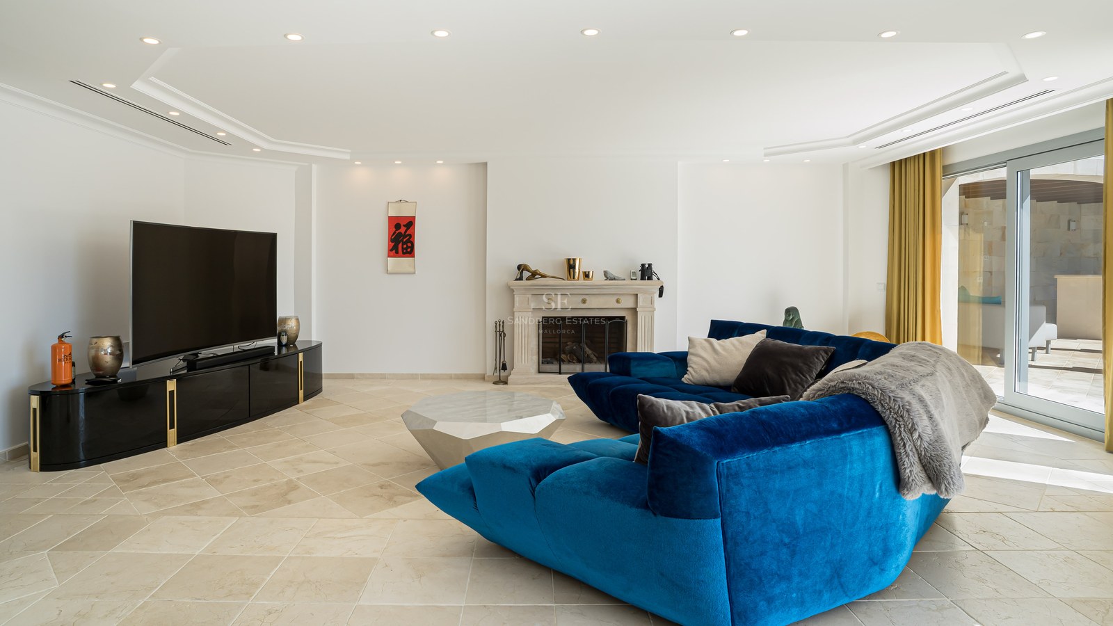 Espace de vie moderne avec un grand canapé en velours bleu, cheminée en pierre et sol en pierre naturelle.