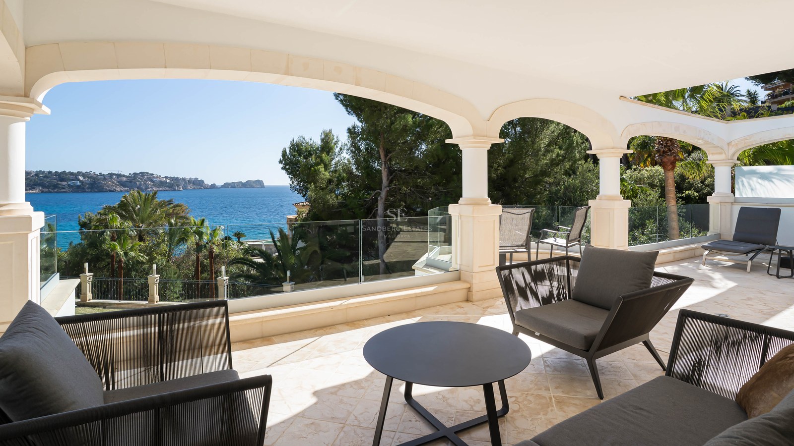 Terrasse couverte en pierre avec arches, garde-corps en verre et mobilier moderne surplombant la Méditerranée.