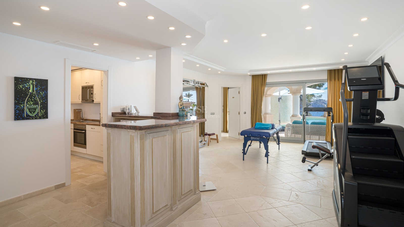 Salle de bien-être lumineuse avec table de massage, équipement de fitness, bar en bois et accès terrasse.
