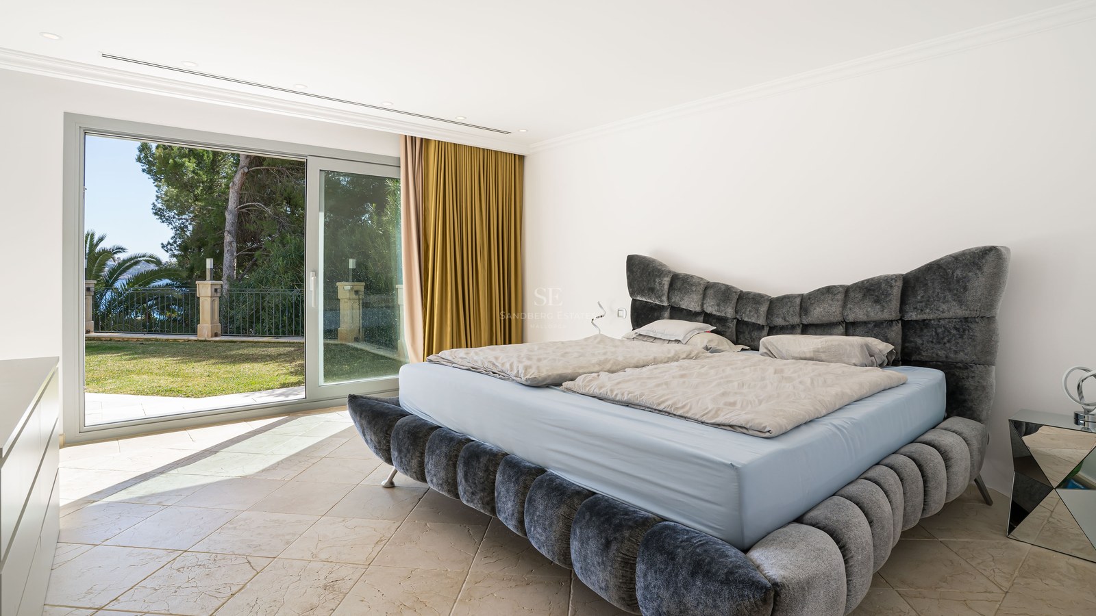 Chambre parentale contemporaine avec lit en velours gris et grandes baies vitrées ouvrant sur le jardin.