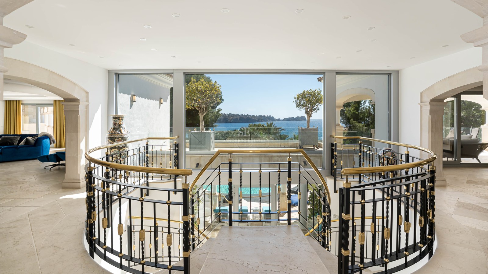 Vue intérieure d'un palier en marbre avec garde-corps orné donnant sur de grandes fenêtres et la mer Méditerranée.