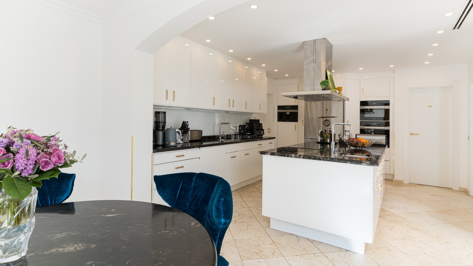 Cuisine contemporaine blanche avec plans de travail en pierre noire, îlot central et chaise en velours bleu.