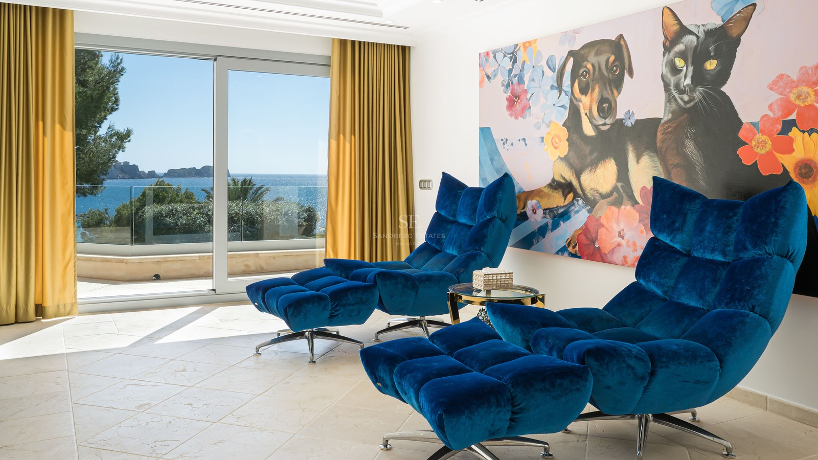 Deux fauteuils de salon en velours bleu avec repose-pieds dans une pièce lumineuse offrant une vue sur la mer.