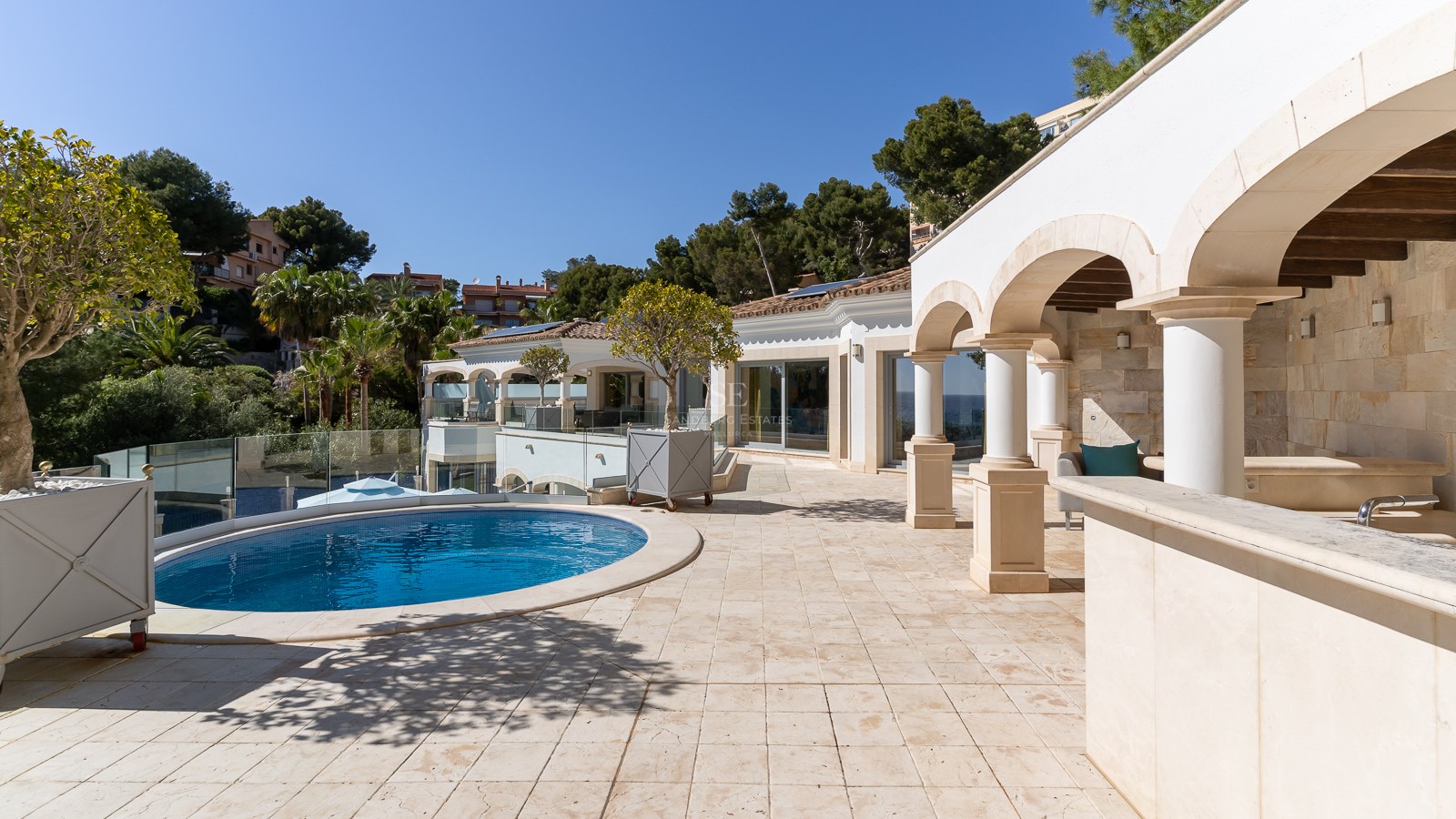 Terrasse de luxe avec sol en pierre, colonnes cintrées et piscine circulaire bleue par temps clair.