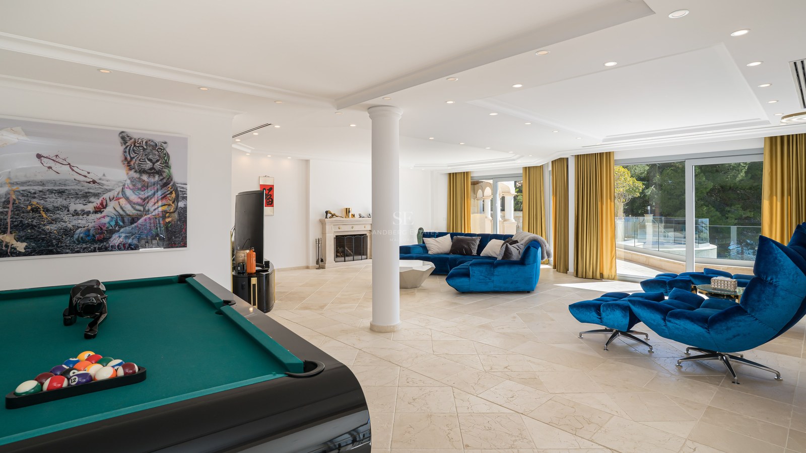 Grande salle de jeux moderne avec canapé bleu, table de billard, sol en pierre et cheminée classique.