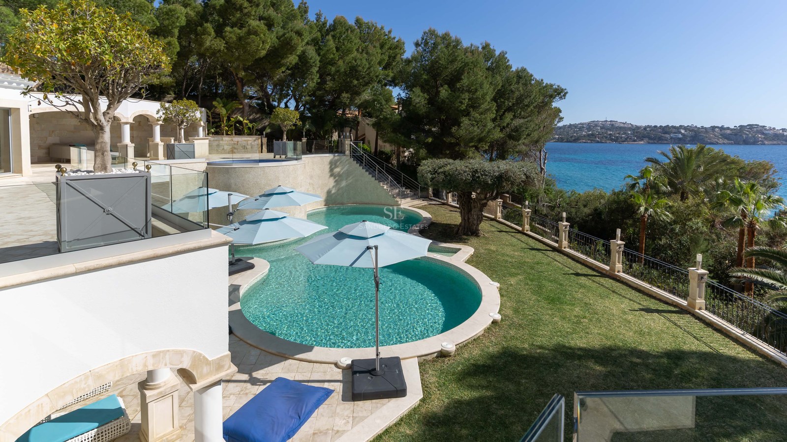 Vue en plongée d'une piscine turquoise aux formes courbes entourée d'un jardin paysager face à la mer.