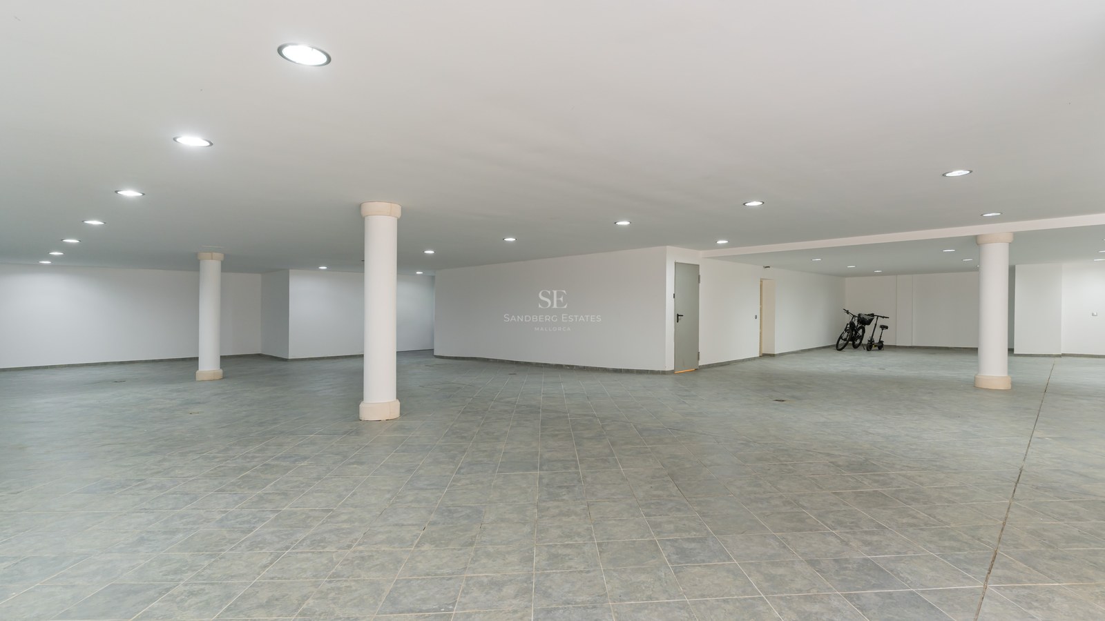 Espace de stationnement souterrain avec carrelage gris, murs blancs, éclairage LED encastré et piliers blancs.