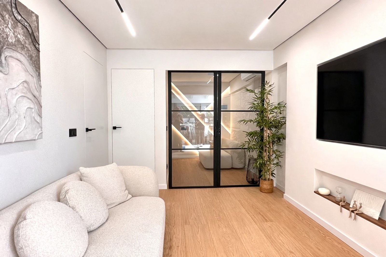 Modern living room featuring a white textured sofa, light wood floors, and black-framed glass double doors.
