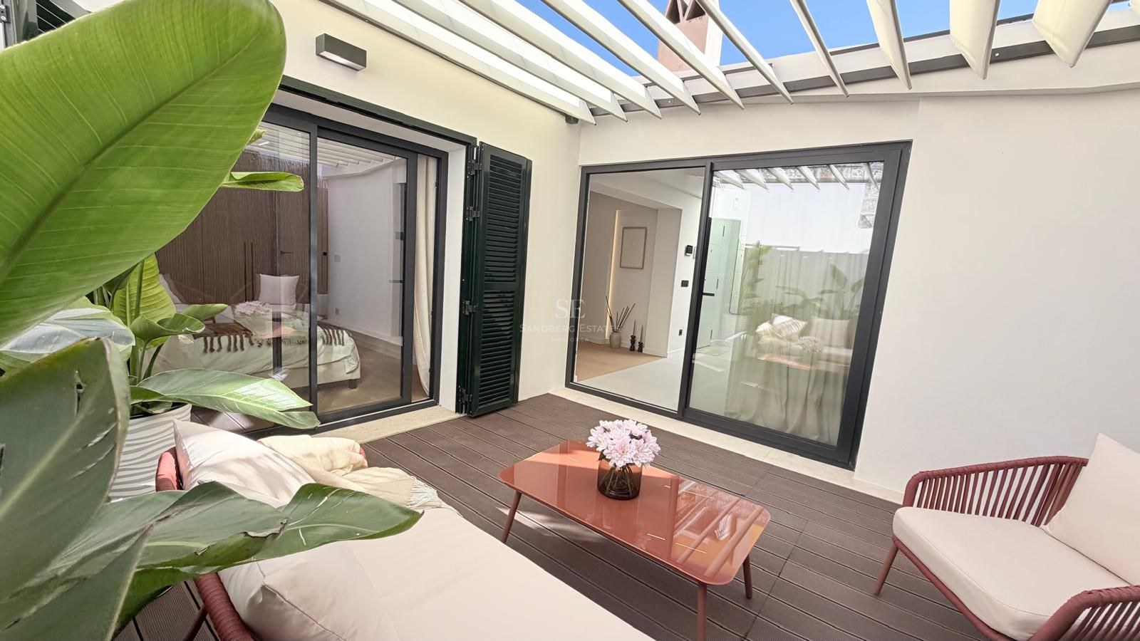 Outdoor patio with white pergola, wooden deck, terracotta-colored furniture, and tropical plants.