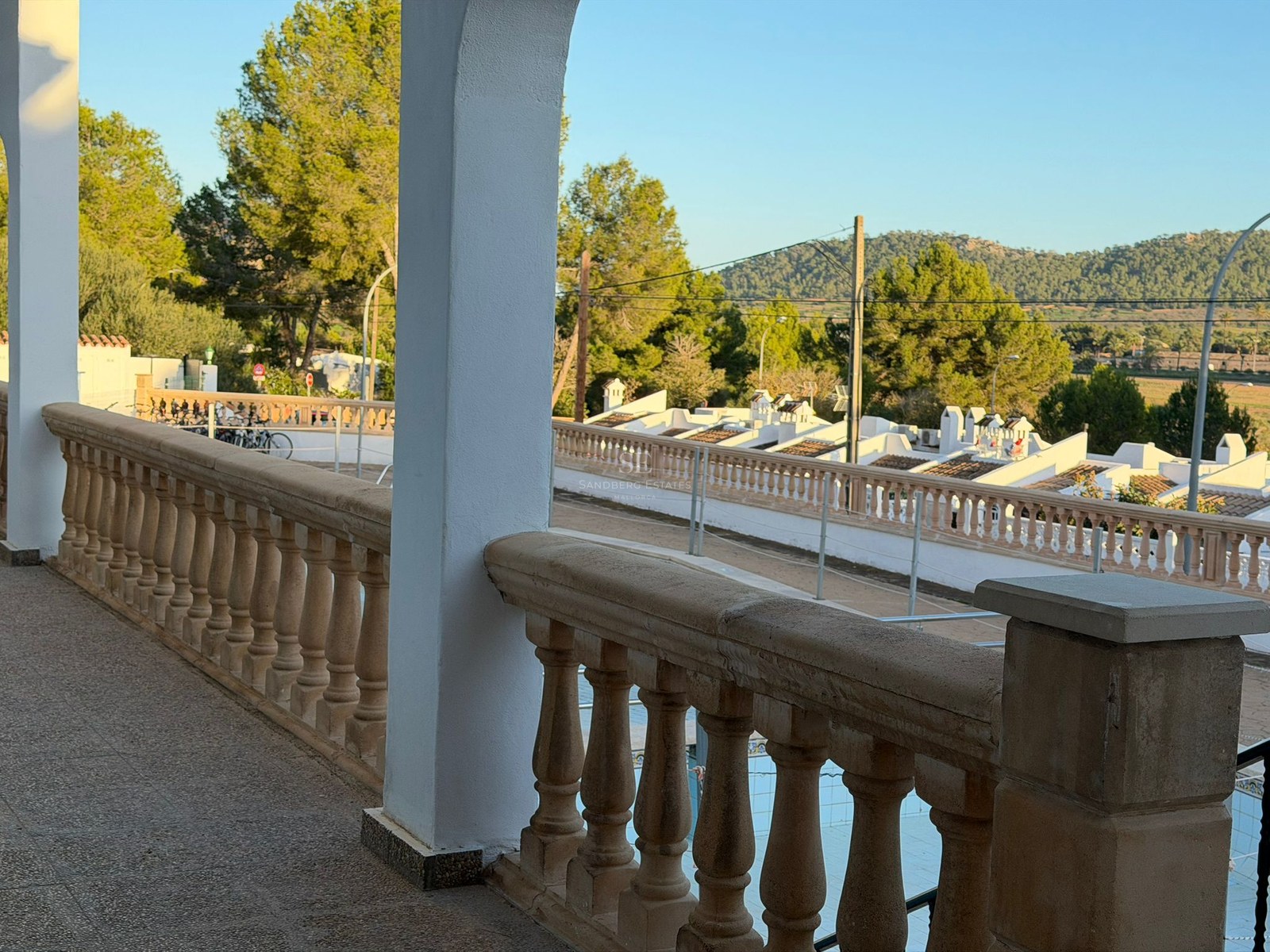 View from a stone balustrade balcony overlooking a Mediterranean neighborhood with white houses and green hills.